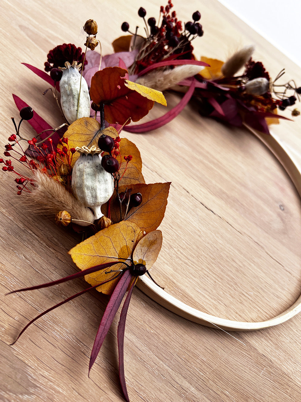Holzring mit getrockneten Blumen, Blättern und Beeren in herbstlichen Farben