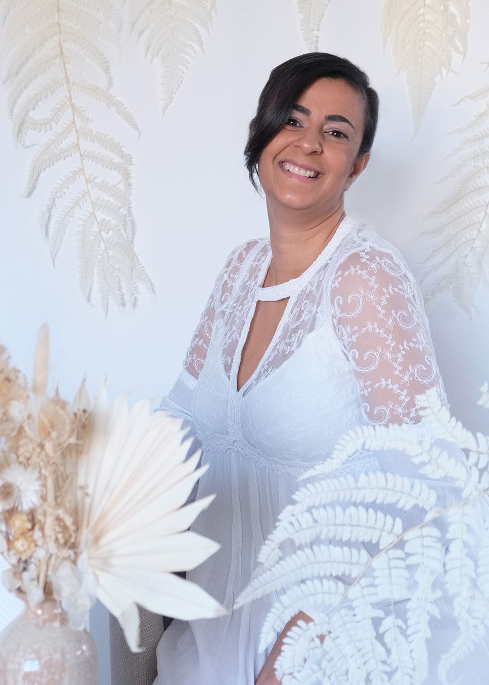 Frau mit weißem Kleid, Trockenblumenstrauß vor ihr und im Hintergrund Farne
