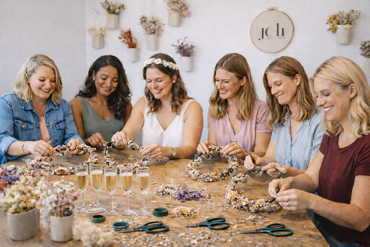 Sechs Frauen sitzen im Workshopraum von JOLI und binden Blumenkränze mit getrockneten Blumen und Bastelmaterialien